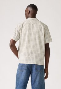 Korte mouwen overhemd in lichtbeige stof met een ruitpatroon in blauw en donkerpaars. Losse pasvorm met een puntkraag en een rugpand.