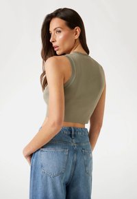 Olivgrön kort topp med ribbat nacke, matchad med högmidjade ljusblå denimjeans med bakfickor och blekt utseende.