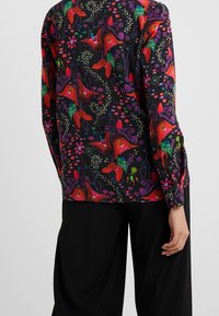 Chemise à manches longues en tissu noir avec un motif floral et d'oiseaux multicolores. Poignets boutonnés et coupe décontractée.