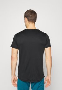 Man with short brown hair wearing a plain black short-sleeve shirt and blue pants, facing away with "stay wild" tattoo on left arm.