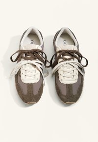 Hnědé a šedé sportovní boty se kombinací texturované semišové kůže a textilu, s bílými tkaničkami a vlnitým zdobením na jazyku.