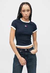 Μπλε σκούρο κοντομάνικο μπλουζάκι με λευκή ριμπ λεπτομέρεια και μικρό λογότυπο στο στήθος, παρουσιάζοντας εφαρμοστή σχεδίαση και ριμπ υφή.