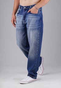 Helle Jeans aus Denim mit lockerer Passform, die verblasste Stellen, normale Taschen und einen Knopfverschluss aufweisen. Tragen mit weißen Sneakers.