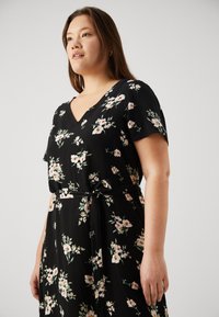 Svart blomsterkjole med korte ermer, V-hals og knyting i midjen. Har små, flerfargede blomster og en flytende stoffkvalitet.