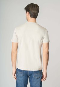 T-shirt in cotone beige con collo rotondo e maniche corte, abbinato a jeans di denim blu. Design visibilmente semplice e texture morbida.