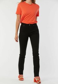 T-shirt corail à manches courtes, jean noir ajusté et sandales à talons blocs rouges avec des accents tissés. Design simple, textures lisses.