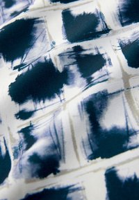 Tkanina o granatowo-białym abstrakcyjnym wzorze z efektem pociągnięć pędzla; gładka tekstura; kwadratowy, siatkowy wzór z jasnymi akcentami.