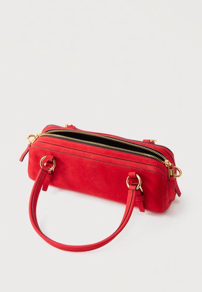 Κόκκινη ορθογώνια γυναικεία τσάντα με χρυσά φερμουάρ, δύο λαβές προσαρτημένες με χρυσούς κρίκους και λεία υφή δέρματος σε λευκό φόντο.