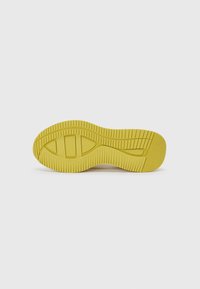 Semelle d'une basket, avec une semelle extérieure en caoutchouc jaune dotée d'un motif de grip texturé et d'un design de bout arrondi et lisse.