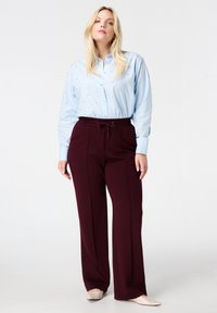 Lichtblauw overhemd met knoopjes en kleine versieringen; maroon wijde broek met een elastische tailleband; beige schoenen.