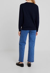Tmavě modrý pletený svetr s kulatým výstřihem a dlouhými rukávy, kombinovaný se světle modrými džínami rovného střihu a černými nazouvacími botami s přezkou.