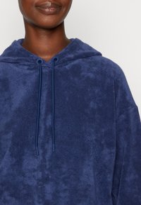 Granatowa bluza z kapturem, wykonana z miękkiej, teksturowanej tkaniny, z sznurkiem przy szyi i luźnym krojem. Prosty design bez wzorów.