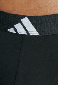 Svart atletisk midjebånd med teksturert overflate som har tre hvite diagonale striper. Stoffet ser glatt og tettsittende ut.