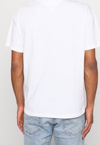 Camiseta de algodón blanca con diseño de cuello en V, mangas cortas y corte relajado, combinada con unos jeans de mezclilla de color azul claro.