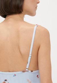 Jasnoniebieska bluzka z tkaniny o prążkowanej fakturze, regulowane ramiączka i kwiatowe wzory. Widok z tyłu pokazuje nisko wycięty fason i dekoracyjne akcenty.