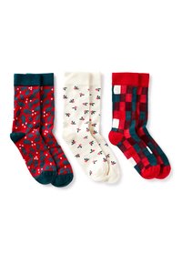 Trzy pary skarpetek: czerwone z nadrukiem ostrokrzewu, kremowe z małymi liśćmi ostrokrzewu oraz w czerwono-zieloną kratę. Wszystkie mają ściągacze i miękką fakturę.