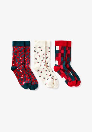 Tres pares de calcetines: rojos con estampado de acebo, crema con pequeñas hojas de acebo y de cuadros rojos y verdes. Todos cuentan con puños acanalados y una textura suave.