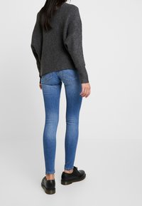 Jersey de punto gris con un corte holgado, combinado con jeans de mezclilla azul ajustados y zapatos negros con cordones. Textura suave, diseño casual.