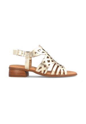 Sandal de piel dorada con diseño recortado, correa en el tobillo ajustable y tacón de madera marrón. Estilo de punta abierta con detalles intrincados.