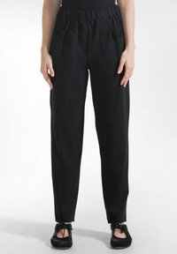 Pantaloni cu talie elastică neagră și buzunare laterale. Prezintă o textură netedă și un design cu picior conic, potriviți pentru purtare casual.