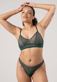 Vihreä verkkomallinen bralette, jossa on kolmiomaiset kupit ja säädettävät olkaimet, yhdistettynä yhteen sopiviin vihreisiin verkkomaisiin alushousuihin, joissa on violetti yksityiskohta vyötäröllä.