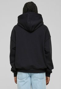 Black oversized hoodie with a drawstring hood, raglan sleeves, and ribbed cuffs. Textured fabric, paired with light blue jeans.