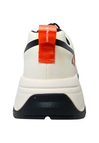 White athletic shoe with a black sole, orange heel tab, and contrasting black stripes on the upper. Textured surface and rounded design.