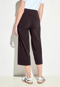 Schwarze Cropped-Hosen mit einem elastischen Bund, zwei Gesäßtaschen, glatter Textur und lässiger Passform, kombiniert mit weißen Sneakers.