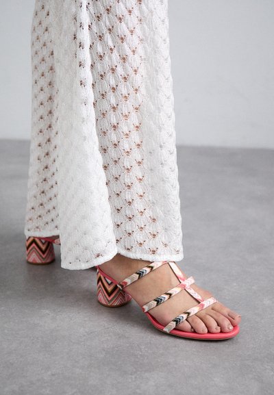 Mångfärgad klacksandaler med rosa remmar och en zigzag-mönstrad klack. Bärs med vita virkning vida byxor.