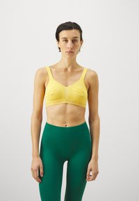 Gul sportsbh med teksturert stoff og brede stropper, med et rosa merke-bånd. Kombinert med høytaljede grønne leggings.