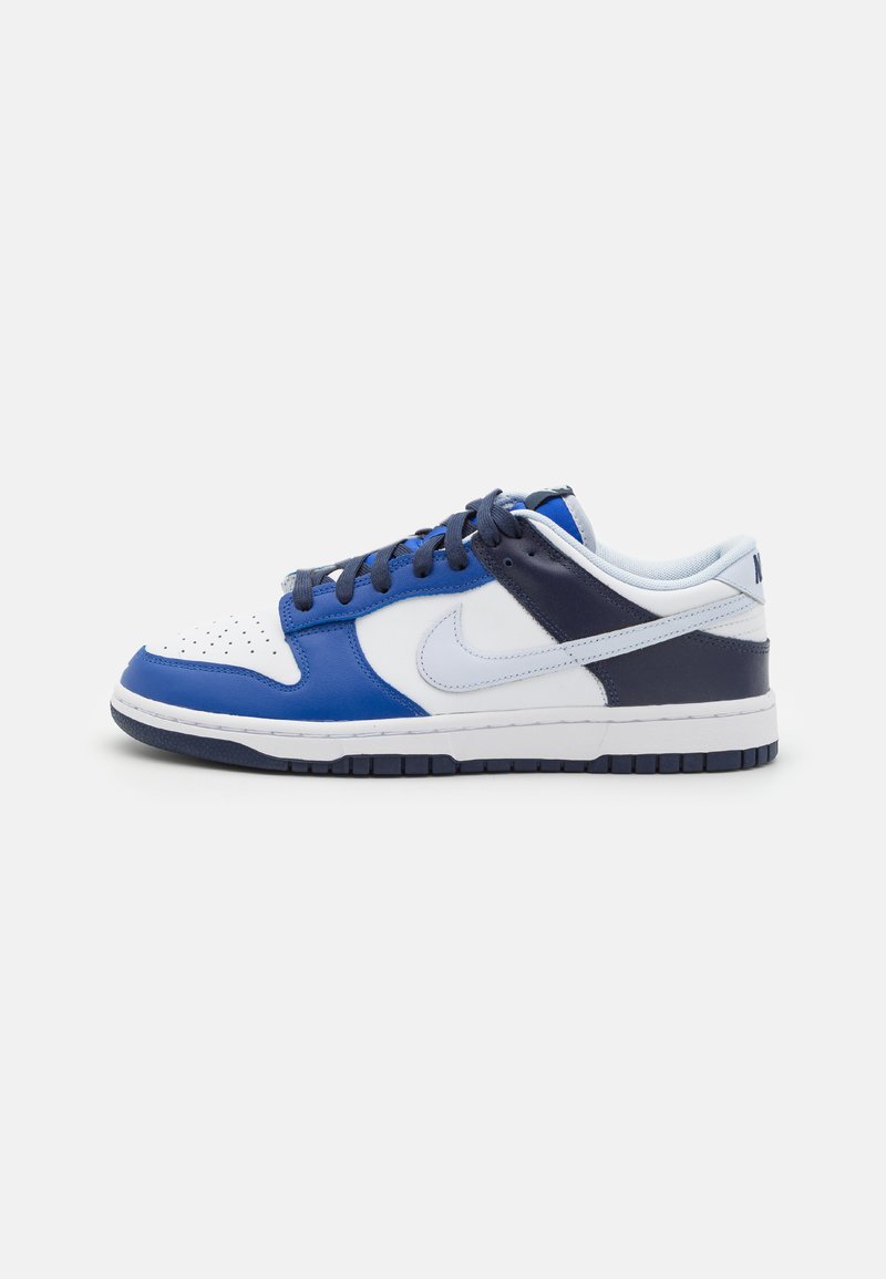 Alacsony sneaker fehér, kék és tengerész-kék bőr panelekből, tengerész-kék fűzőkkel és fehér Nike logóval fehér háttéren.