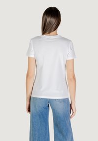 T-shirt bianco in cotone con scollo rotondo classico, maniche corte e silhouette aderente. Il modello lo abbina a jeans a gamba larga di colore blu chiaro.