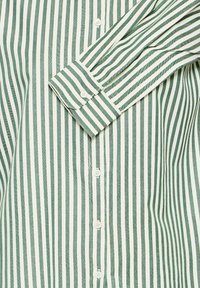 Camicia a maniche lunghe a righe verdi e bianche, con bottoni sul davanti e ai polsini, realizzata in tessuto leggero.