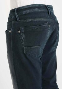 Jean en denim foncé avec une finition délavée, dotée de deux poches arrière avec quincaillerie en métal. Conception slim fit avec une taille mi-haute.