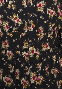 Tissu noir avec un motif floral de fleurs rouges, jaunes et blanches, et de petits boutons noirs au centre.