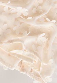Crèmekleurige doorschijnende stof met geborduurde doorzichtige bloemen in een delicate, lichte textiel van dichtbij.