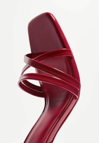 Sandale à talons hauts rouges avec un design à bout carré, fabriquée dans un matériau en verni brillant et dotée de plusieurs brides croisées pour le soutien.