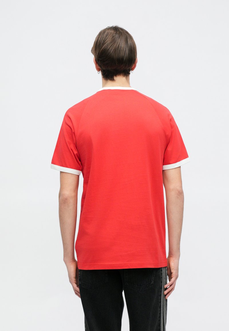 T-shirt rossa a maniche corte con bordo bianco attorno al collo e alle maniche, caratterizzata da una vestibilità comoda e una texture di cotone liscia.