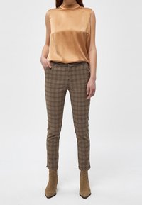 Satin, ärmlös topp i ljusguld; rutiga, figurnära byxor i bruna, svarta och krämfärgade nyanser; ihop med beige ankle boots.