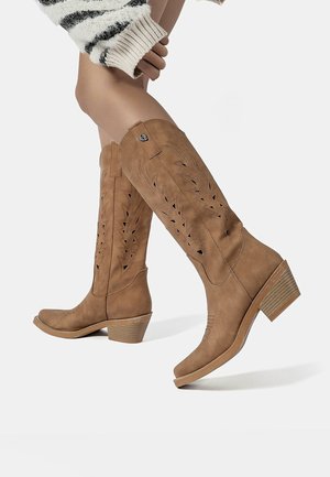 Tan laarzen tot halverwege het scheenbeen met uitgezaagde bladerenpatronen, ronde neus en gestapelde hak. Gemaakt van suède-achtig materiaal. Verstelbare riempjes bovenaan.