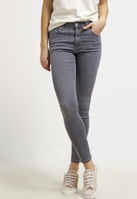 Grå slim-fit jeans med femficksdesign, dragkedja och lätt stretch. Kombineras med ljusa casual sneakers.