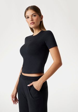 Camiseta negra recortada de tejido suave, con mangas cortas y escote redondo. Combinada con pantalones negros de cintura elástica a juego.