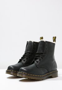 Bottes basses en cuir noir avec bout rond, lacets à l'avant et surpiqûres jaunes. Surface texturée et languette de traction à l'arrière.
