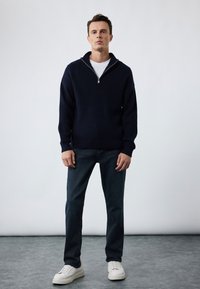 Suéter de punto en azul marino con cuello con cremallera, combinado con jeans de mezclilla oscura y zapatillas blancas, con un ajuste relajado y textura acanalada.