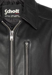 Zwarte leren jas met een zilveren ritssluiting aan de voorkant, een zijritszak en een reverskraag. De binnenvoering is glad, met een merklabel.