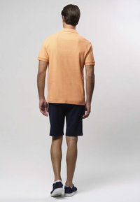 Lühikeste varrukatega polo-särk heledas oranžis, sirge ääre ja kraega, koos tumeliste sportlike jalanõude ja tumesiniste lühikeste pükstega.