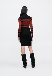 Robe à col roulé rayée noire et rouge, ajustée, texture côtelée, longueur genou, associée à des bottes noires décontractées montant jusqu'au genou.