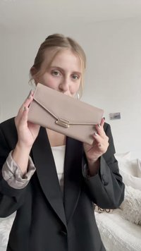 Clutch de imitación cuero beige con solapa plegable, presentando un cierre metálico y detalles de costura. Textura suave, forma rectangular.