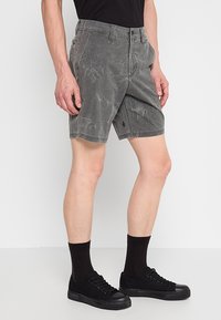 Shorts en coton gris avec un motif texturé décoloré. Comprend une fermeture à bouton, des poches avant et un petit logo sur l'ourlet. Associés à des chaussures noires.