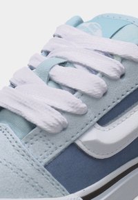 Αθλητικό παπούτσι σε ανοιχτό μπλε και άσπρο χρώμα με χοντρές λευκές κορδέλες, υφές από σουέτ και ύφασμα, και ορατό λογότυπο της μάρκας στη γλώσσα του παπουτσιού.